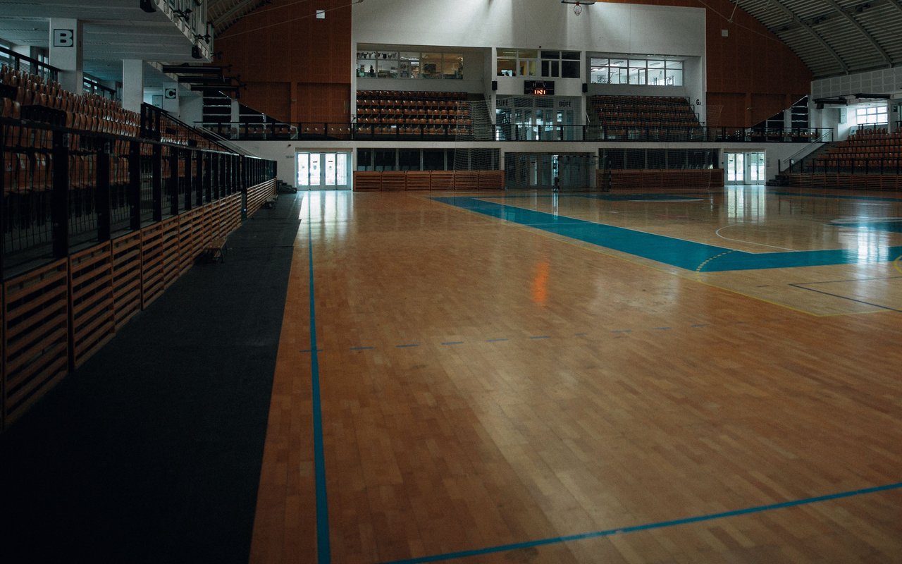 Pusta hala sportowa z drewnianym parkietem i drewnianymi barierkami przy trybunach