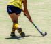 A young player dribbling the ball with the stick close to the ground on an artificial turf pitch