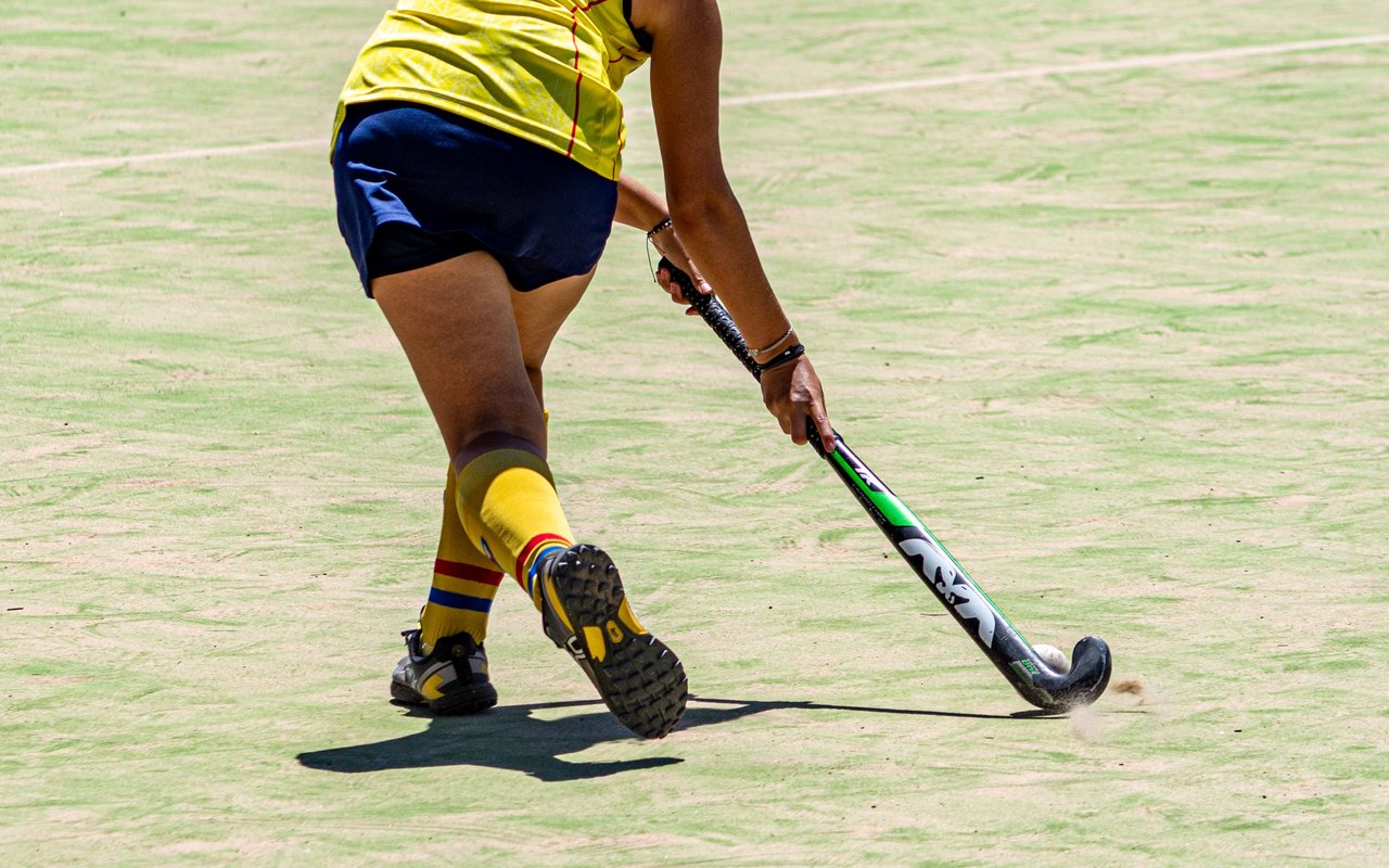 A young player dribbling the ball with the stick close to the ground on an artificial turf pitch